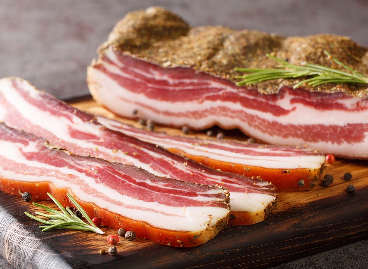 Dry-cured pork belly bacon with spices and rosemary close-up on a wooden board on the table. horizontal